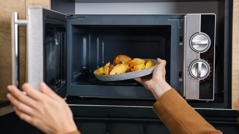Person placing a dish of potatoes, vegetables, and meat in the microwave