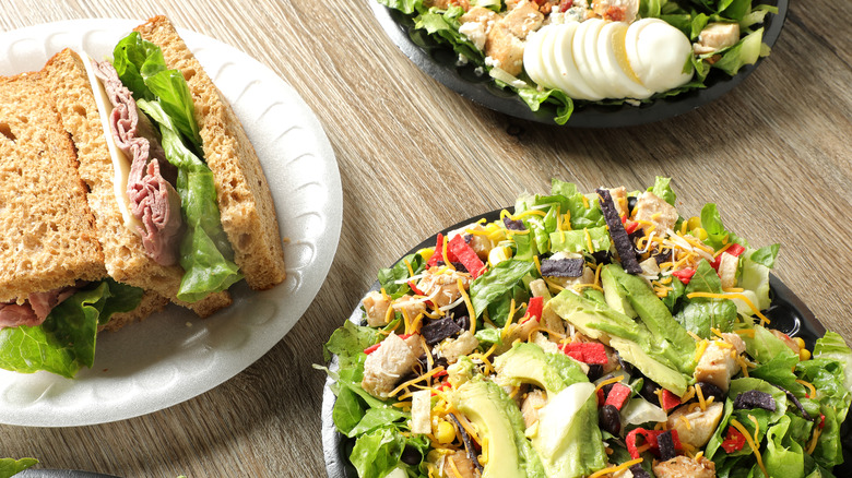 Roast beef sandwich on a plate beside two bowls of salad
