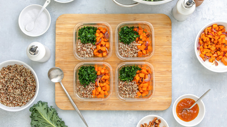 Four identical dishes of quinoa, sweet potatoes, and kale on a cutting board