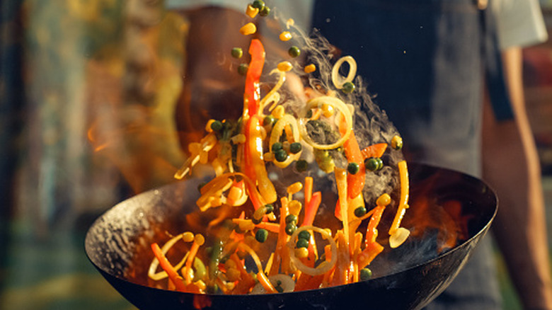 Cook tossing vegetables in a wok while making stir fry