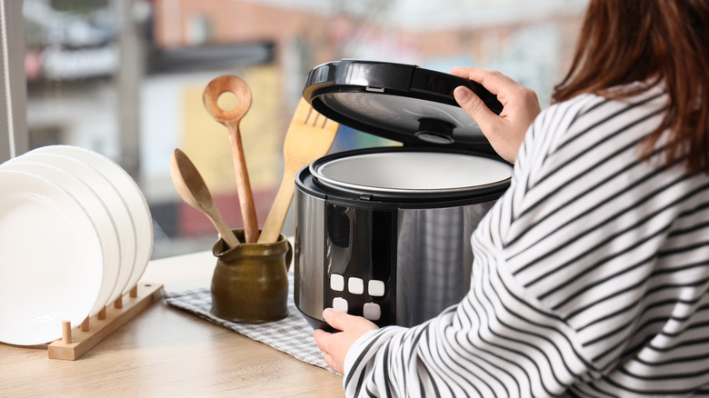 Person opening an electric rice cooker on the kitchen counter