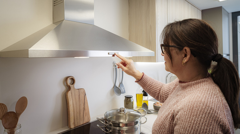 Woman presses the button to turn on a hood fan above the stove