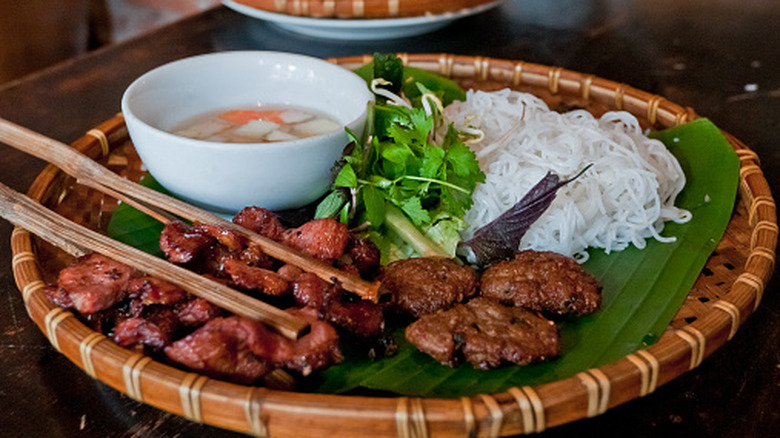 Platter of Vietnamese bun cha, with grilled meats, fresh herbs, cold vermicelli noodles, and nuoc mam