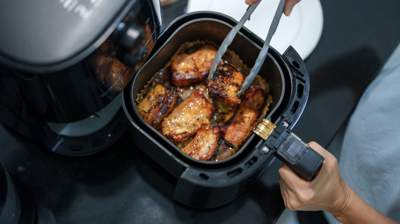 Person holding the basket of an air fryer and plucking out a piece of meat using tongs