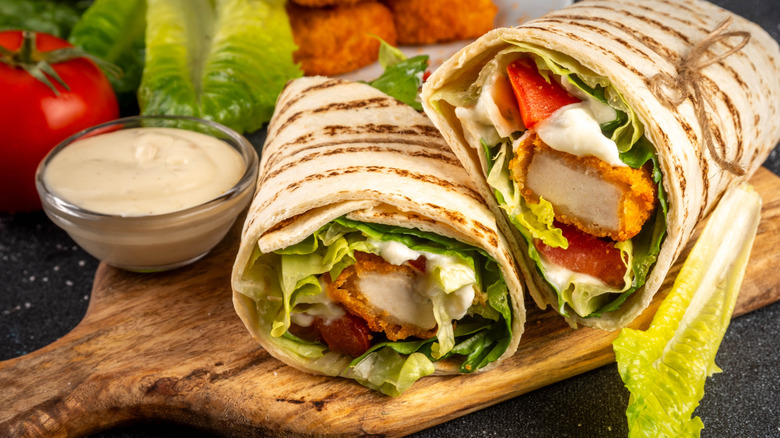 Crispy chicken salad wraps on wooden board with small bowl of creamy sauce