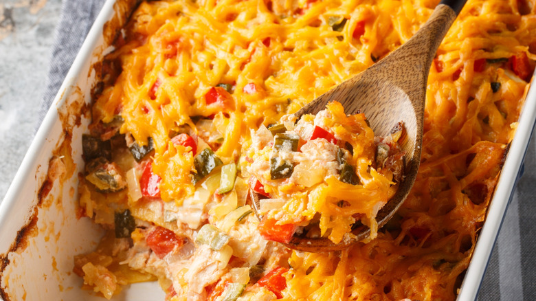 Spooning cheesy chicken and veg casserole out of baking dish