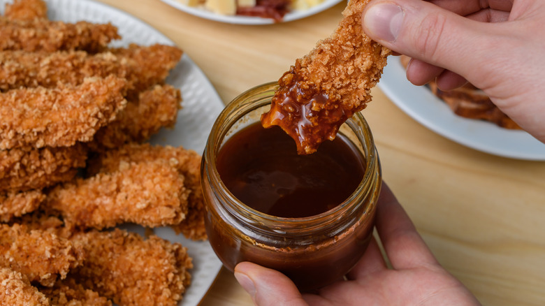 Dipping crispy chicken tenders into pot of bbq sauce