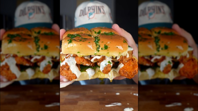Hands holding crispy buffalo chicken sliders with ranch sauce