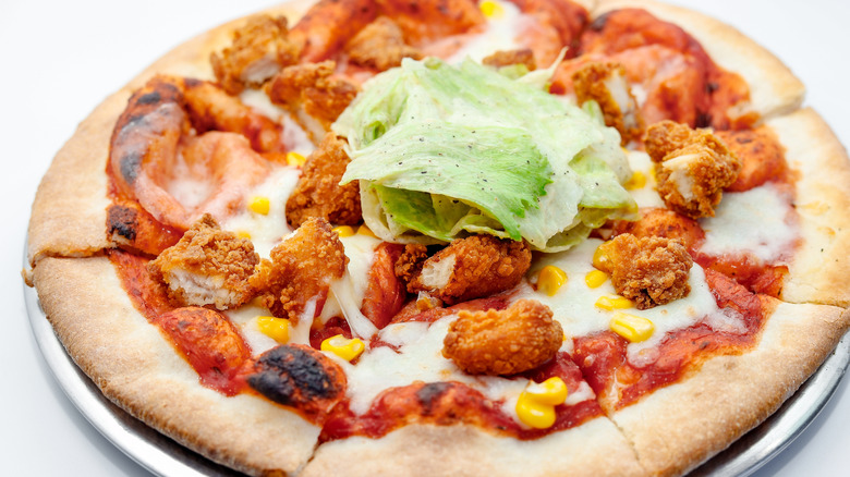 Cheese and tomato pizza topped with crispy chicken pieces, lettuce, and corn