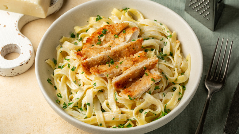 Bowl of alfredo pasta topped with crispy sliced chicken