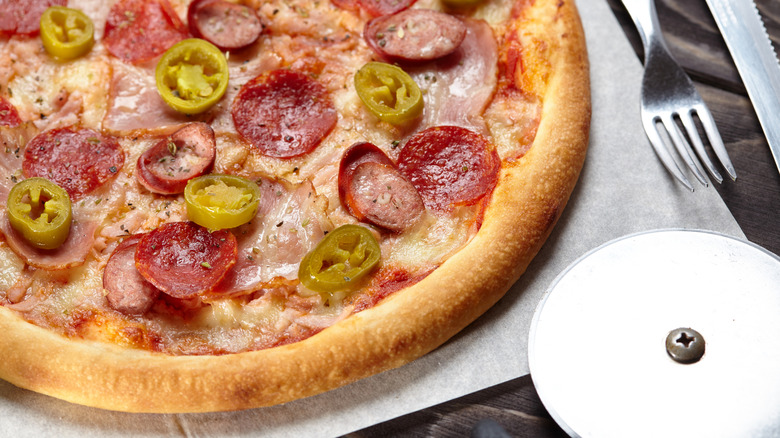 A pizza topped with pepperoni, sausage, ham, and banana peppers