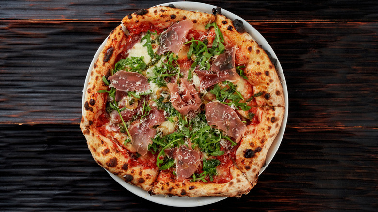 An aerial view of a gourmet pizza topped with flowers made from mortadella