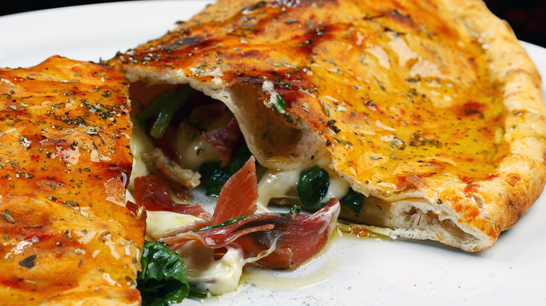 A large calzone cut in half to allow the filling to spill out onto a plate
