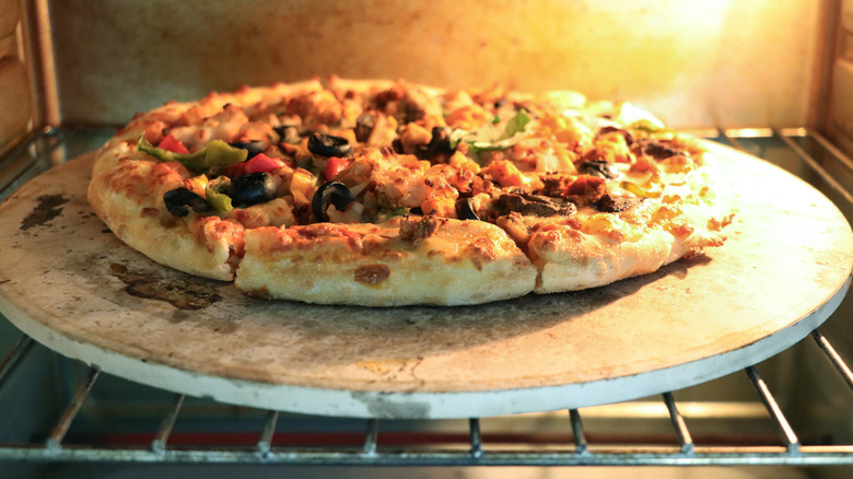 A pizza baking in an oven on a pizza stone