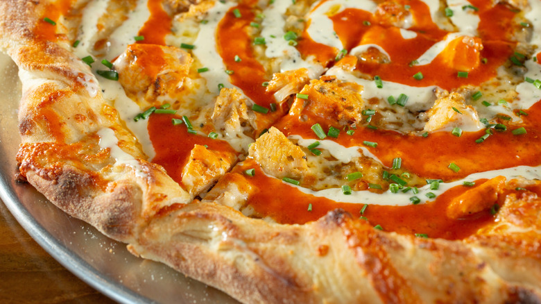 A close-up view of a Buffalo chicken pizza garnished with swirls of ranch dressing and Buffalo sauce