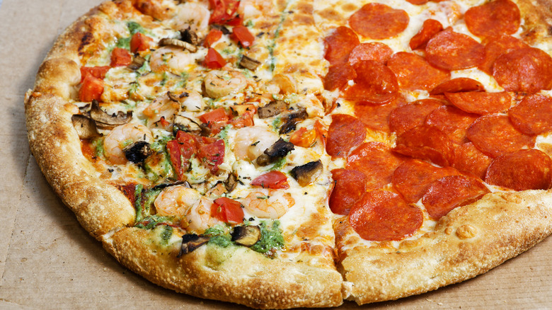A close-up view of a half pepperoni, half supreme pizza in a cardboard pizza box
