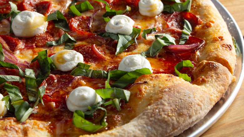 A close-up view of a pepperoni pizza topped with fresh ricotta, basil, and hot honey