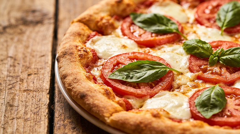 A close-up view of a cheese pizza topped with sliced tomatoes, mozzarella, and basil leaves