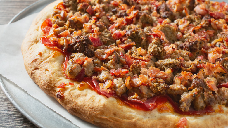 A close-up view of a hearty meat-lover's pizza topped with pepperoni, bacon, ham, and sausage