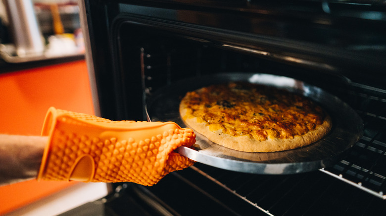 A person wearing orange oven mitts puts a pizza in their oven