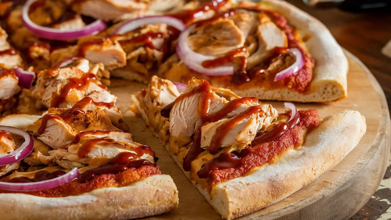 A barbecue chicken pizza being sliced on a wooden cutting board