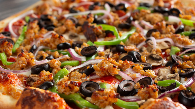 A close-up view of a supreme pizza or Combo Pizza featuring pepperoni, sausage, black olives, red onions, and green bell peppers