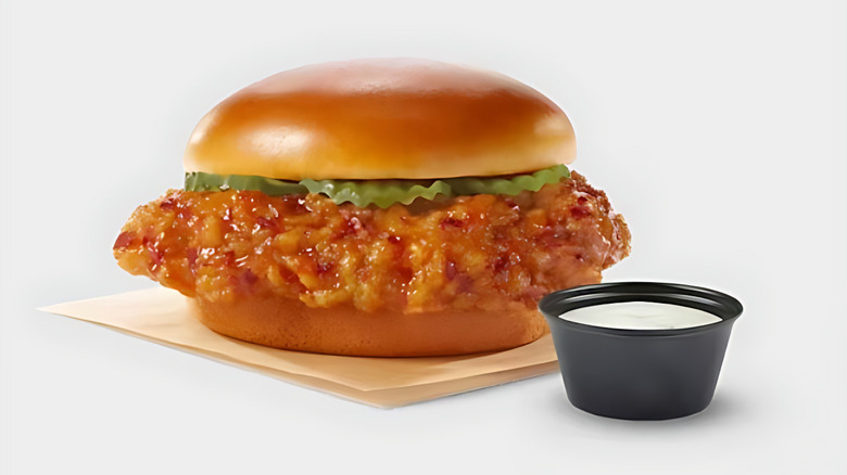 A Wingstop fried chicken sandwich with pickles on a soft bun, served with a side of ranch dressing