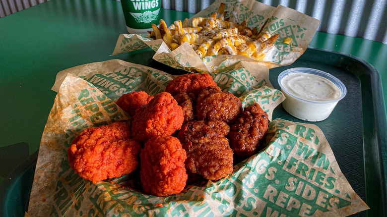 A tray of boneless wings with two flavors, seasoned fries topped with cheese, a side of ranch, and a drink from Wingstop