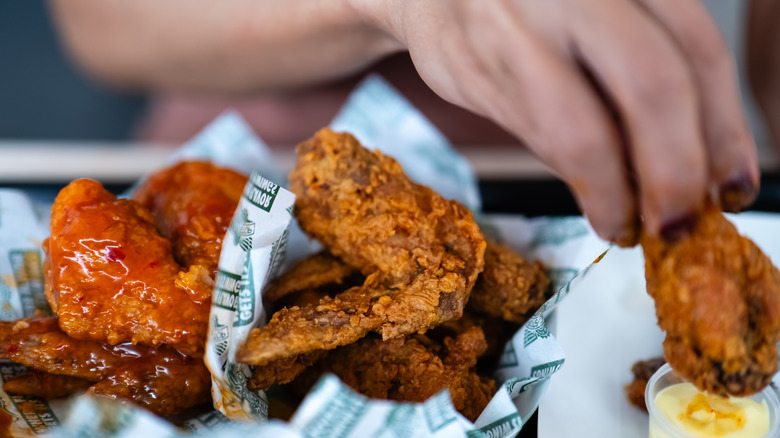A person's fingers holding fried chicken from Wingstop and dipping it in a sauce