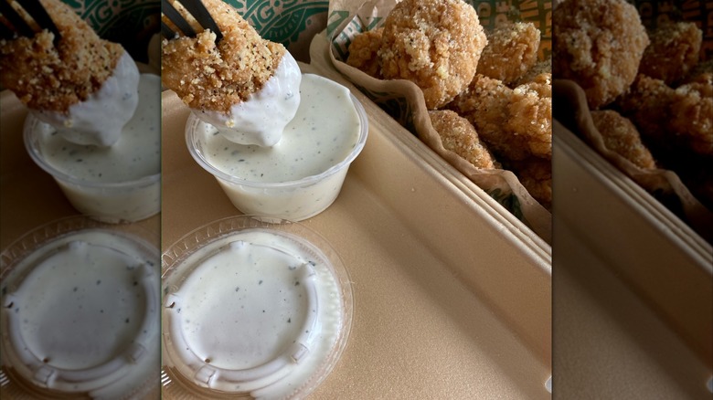 A crispy boneless wing being dipped into a container of creamy ranch sauce from Wingstop