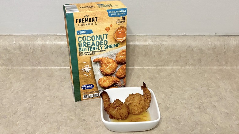 Jumbo coconut breaded shrimp in a box and bowl on neutral background.