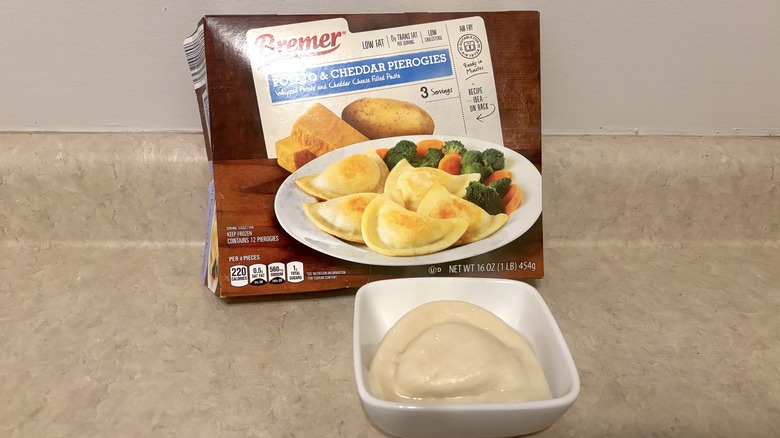 Potato and cheddar pierogies in a box and bowl on a neutral background.