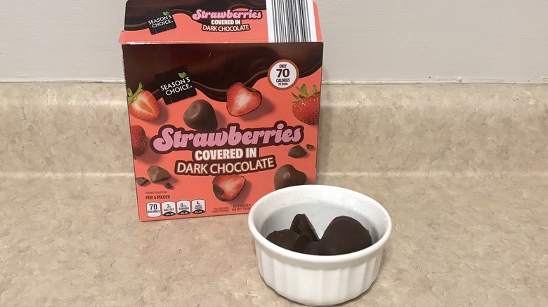 Strawberries covered in dark chocolate in a bowl and box on neutral background.
