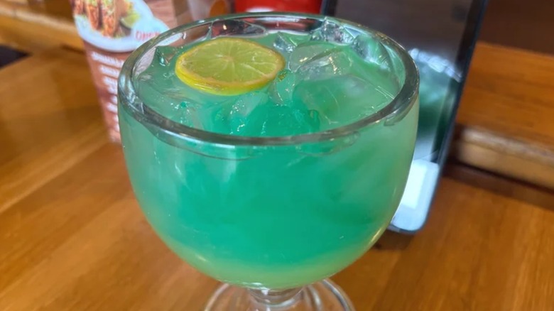 A blue-tinted cocktail in a rounded glass sitting on a wooden table.