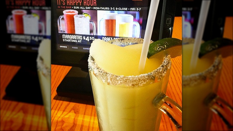 A frozen margarita on a wooden table, in front of a tablet showing images of other margaritas and draft beers.