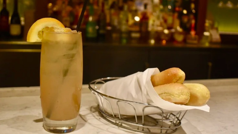 An orange cocktail in a thin glass served on a wooden table with a slice of orange.