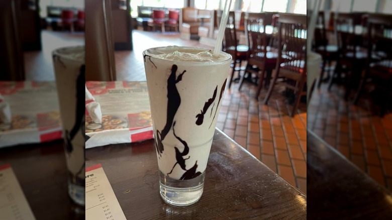 A creamy Frozen Mudslide cocktail, served in a glass swirled with chocolate syrup, sitting on top of a menu.