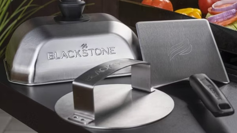 Blackstone 3-piece hamburger grill tool set on grill with vegetables in the background