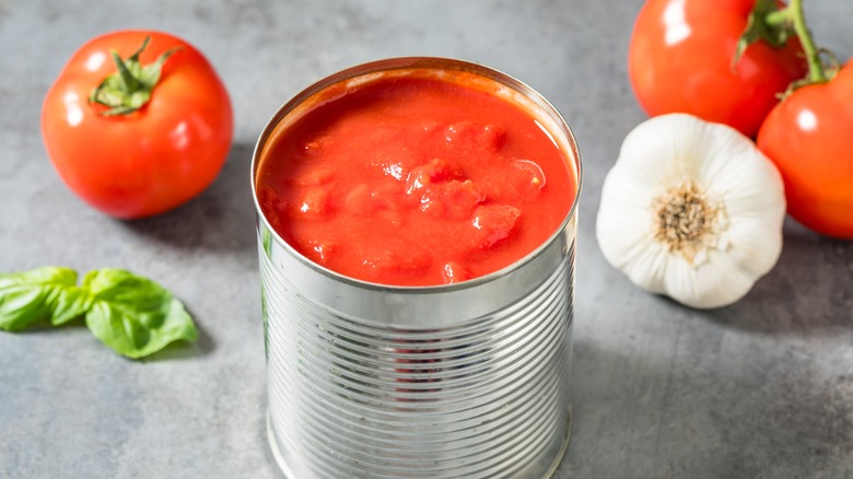 Open can of tomatoes with garlic, fresh tomatoes, and garlic in the background