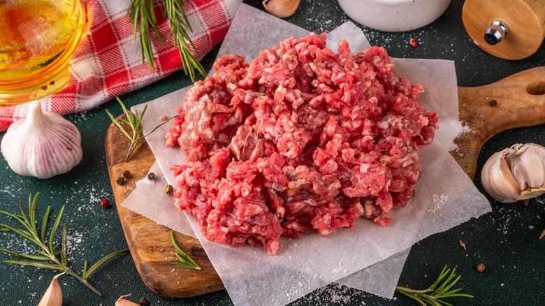 Ground beef on greaseproof paper on top of a wooden board, with garlic and herbs