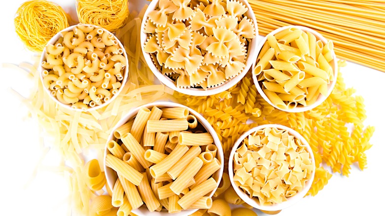 Bowls of various types of dried pasta in white bowls