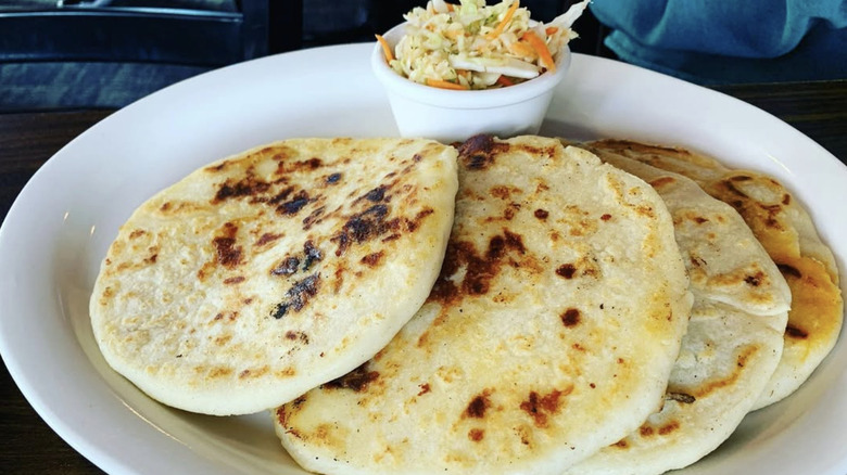 Four layered pupusas with curtido on a white plate