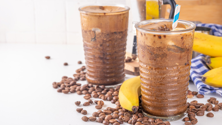 Two cups of frozen banana coffee, among bananas and coffee beans