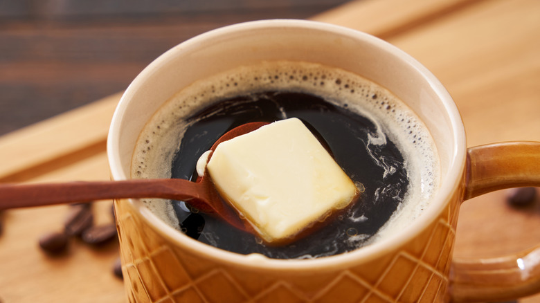 Close-up of a cup of bulletproof coffee, showing butter being added with a spoon