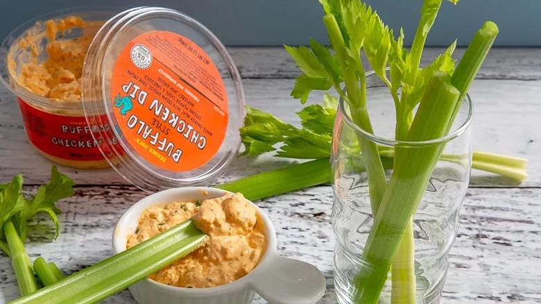 Container of Trader Joe's Buffalo Style Chicken Dip on table, in cup with lots of celery sticks surrounding