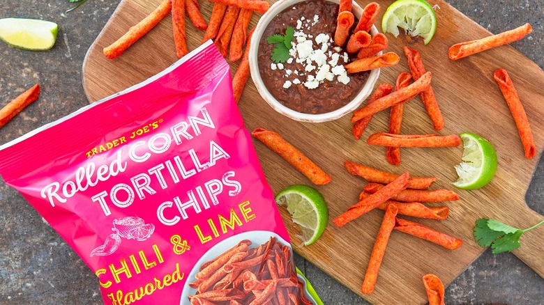 Bag of Trader Joe's Rolled Corn Tortilla Chips next to lime wedges and chips on cutting board with dip