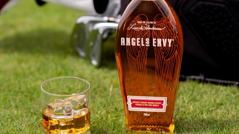 A bottle of Angel's Envy Port Wine Barrel Finish placed on grass in front of golf clubs