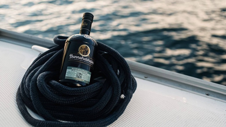 A bottle of Bunnahabhain Stiuireadair posed inside a coil of rope on the side of a boat