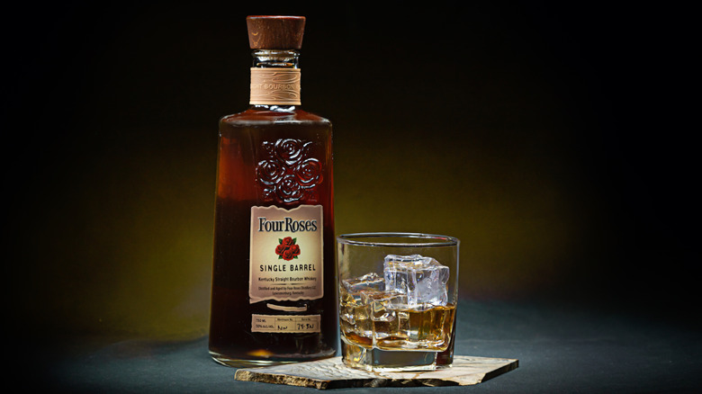 A stylized product shot of a bottle of Four Roses Single Barrel next to a filled glass on a stone slate