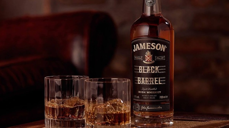 A bottle of Jameson Black Barrel on a table alongside two filled tumbler glasses
